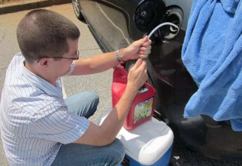 Caucasian man with buzzed hair siphoning gas from a car into a canister