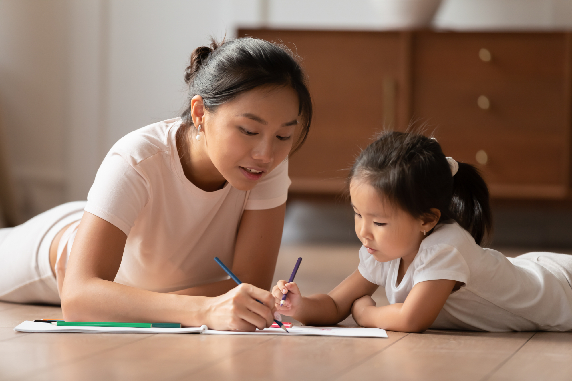 Young Vietnamese nanny drawing with a young girl she watches.