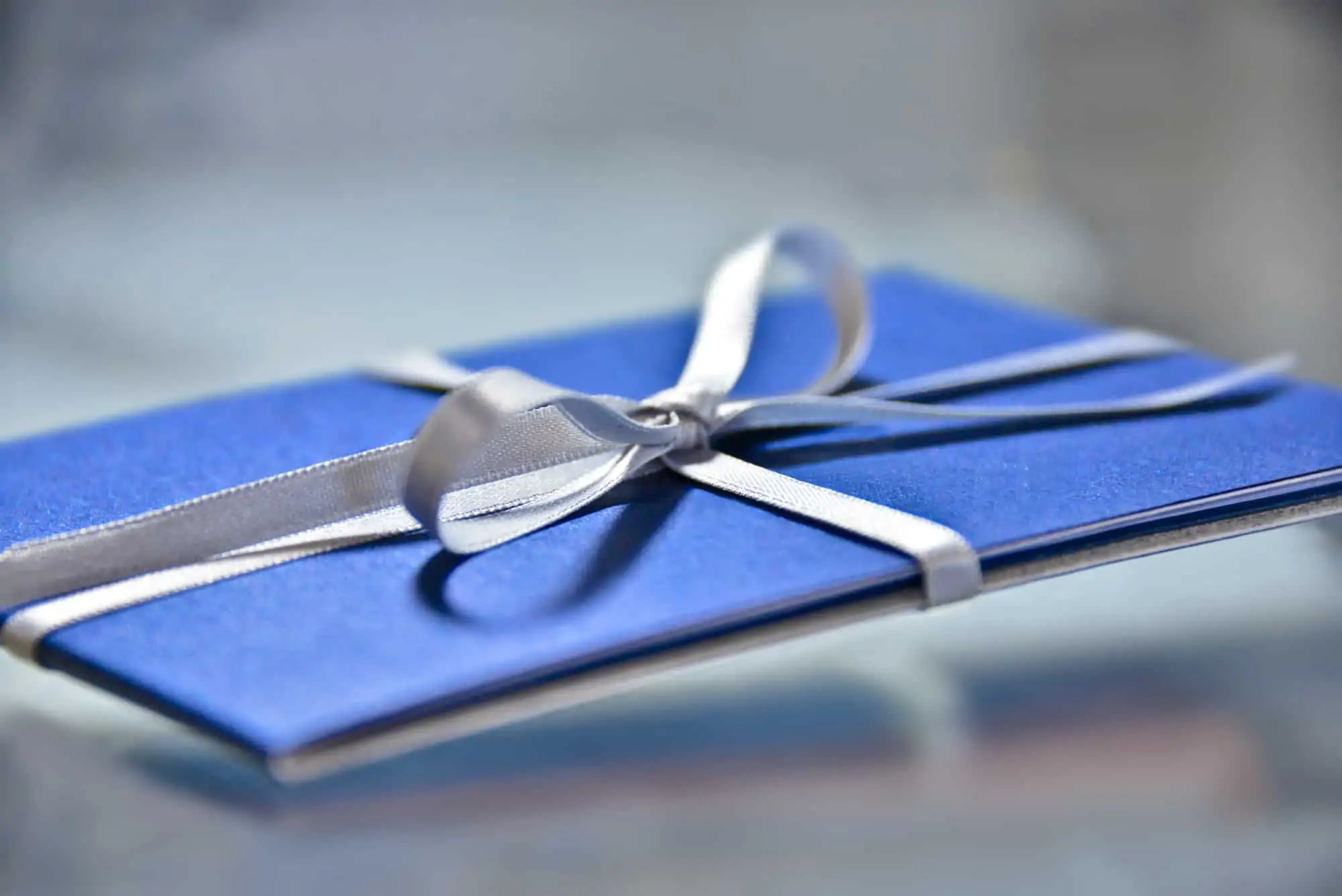 Gift card wrapped in a blue folder with a silver stain ribbon tied in a bow.