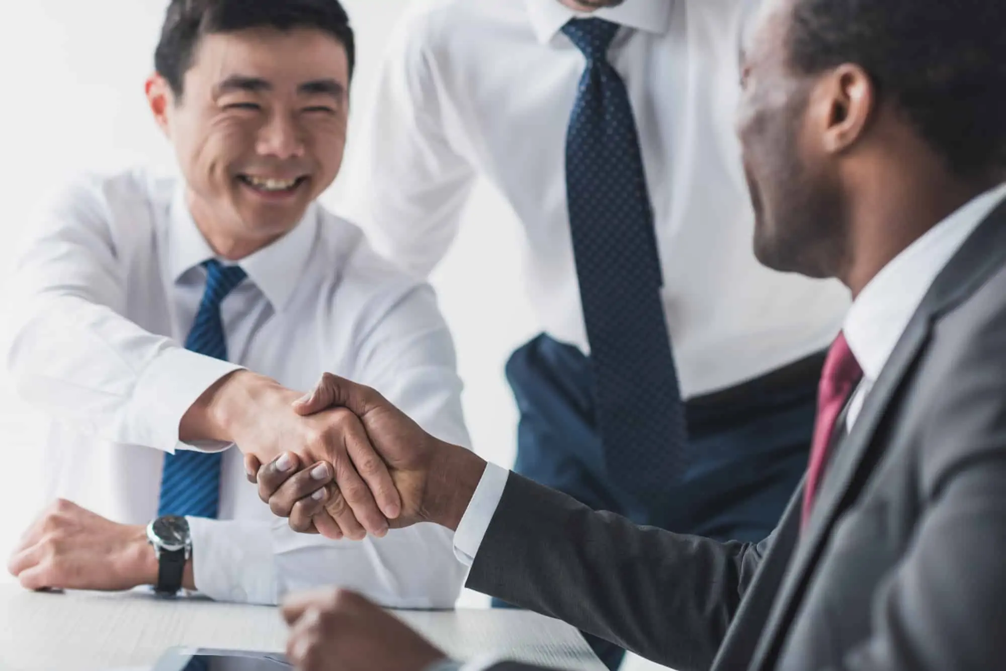 Black male tax accountant with a good personality laughing and shaking hands with East Asian male client